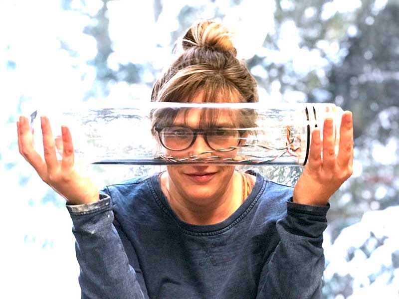 Melissa Omand holds a large, clear glass flask in front of her face. 