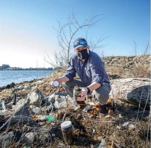 Person collecting samples of plastic on a rocky shoreline